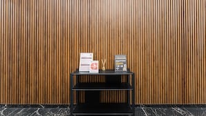 Ein schwarzes Metallregal mit zwei Hinweisschildern vor einer Wand aus Holzlamellen.