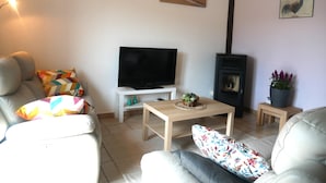 Una sala de estar con un sofá, un televisor, una mesita, una chimenea y un cuadro en la pared.