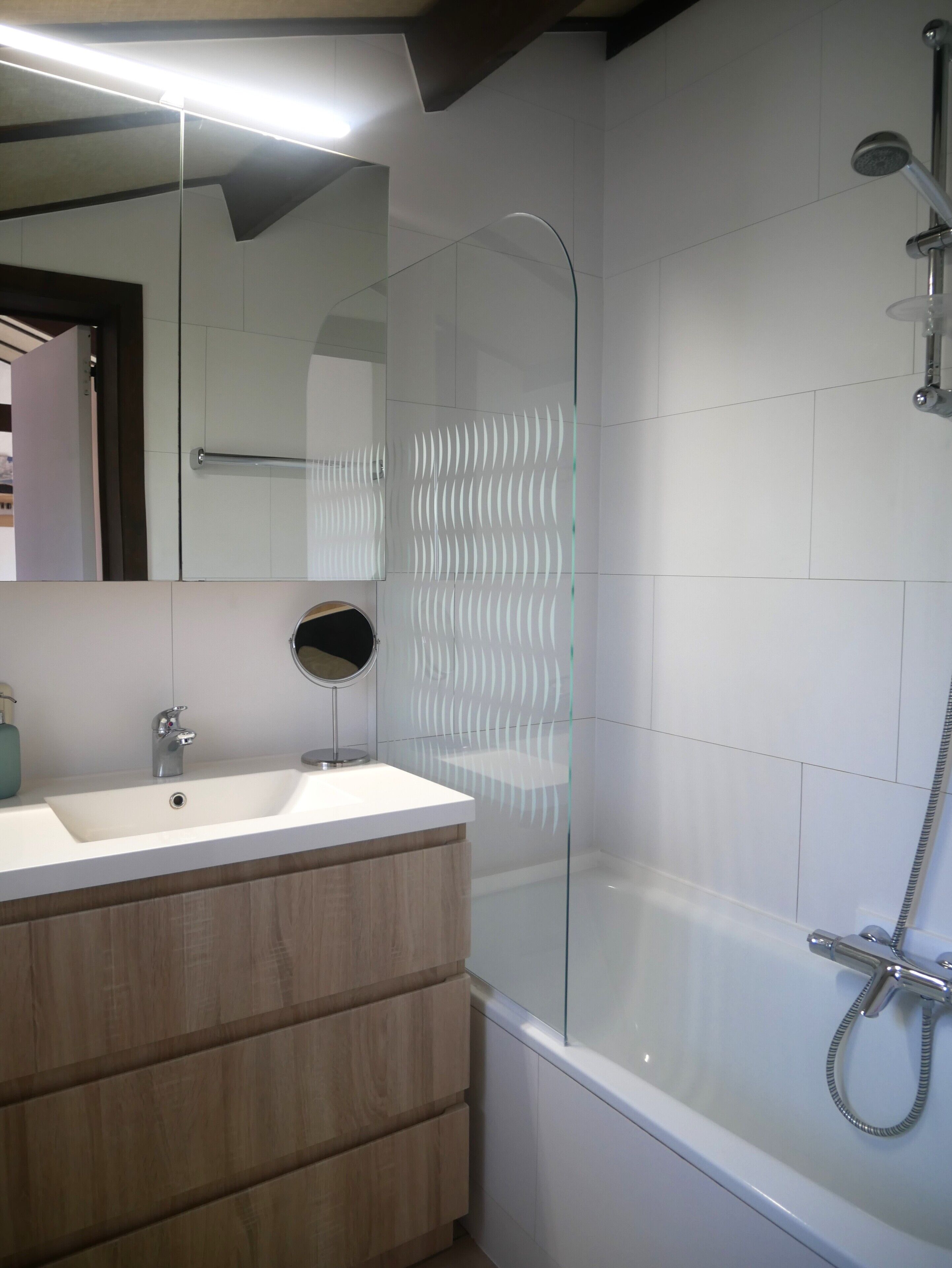 Un bagno moderno con cabina doccia in vetro, un lavandino bianco e un mobile bagno in legno.