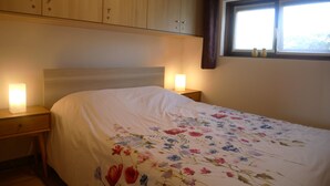 Un dormitorio con cama, armarios de madera, mesita de noche, ventana y lámpara.