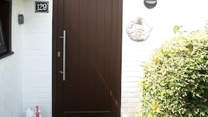 Una puerta marrón con una placa que indica el número 129 y una pequeña decoración de gallina en el suelo.