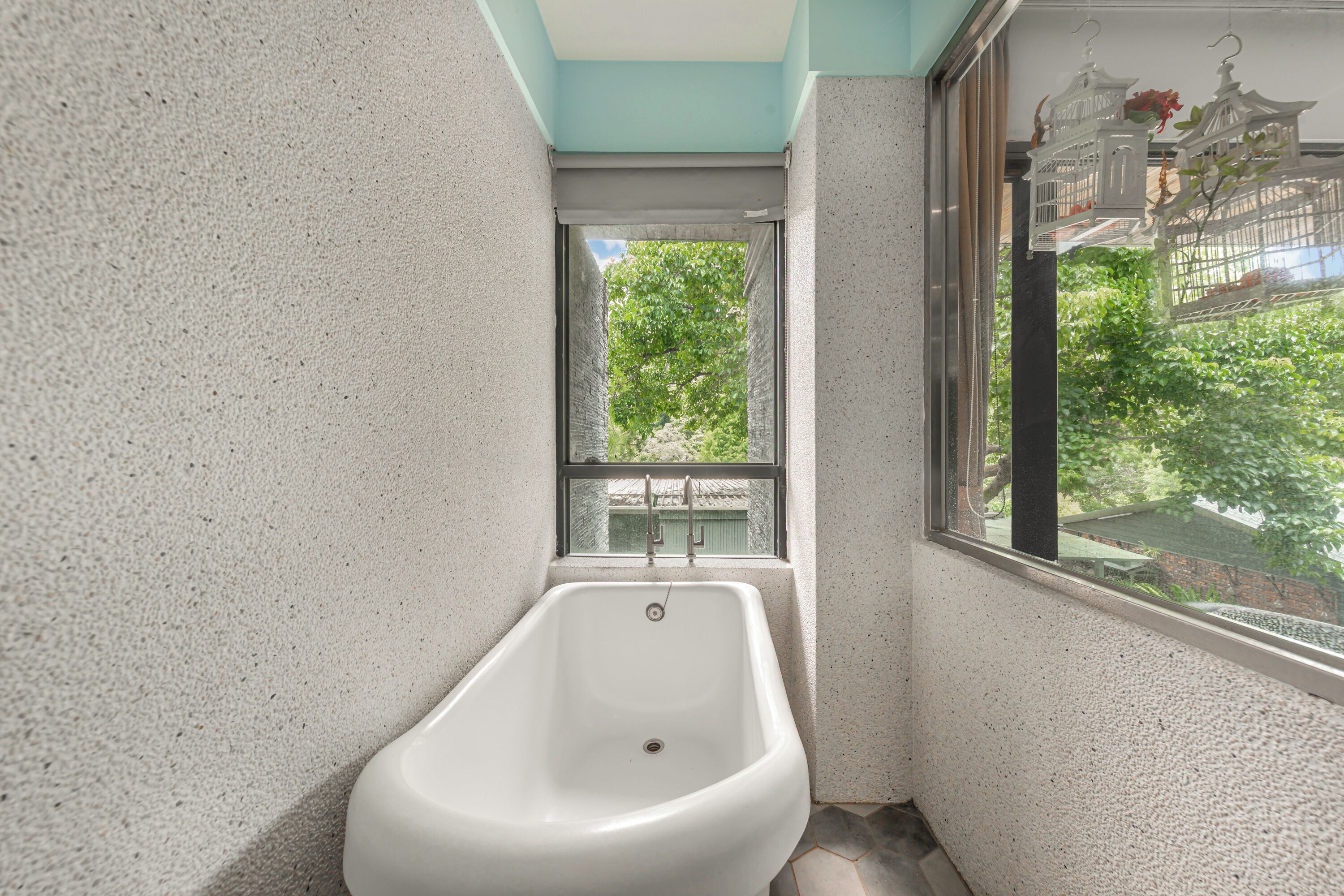 A small, narrow bathroom with a bathtub, a window with a view of greenery, and a birdcage decoration.