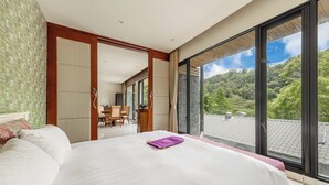 Habitación de hotel con una cama grande, un escritorio y vistas a un paisaje verde a través de grandes ventanales.