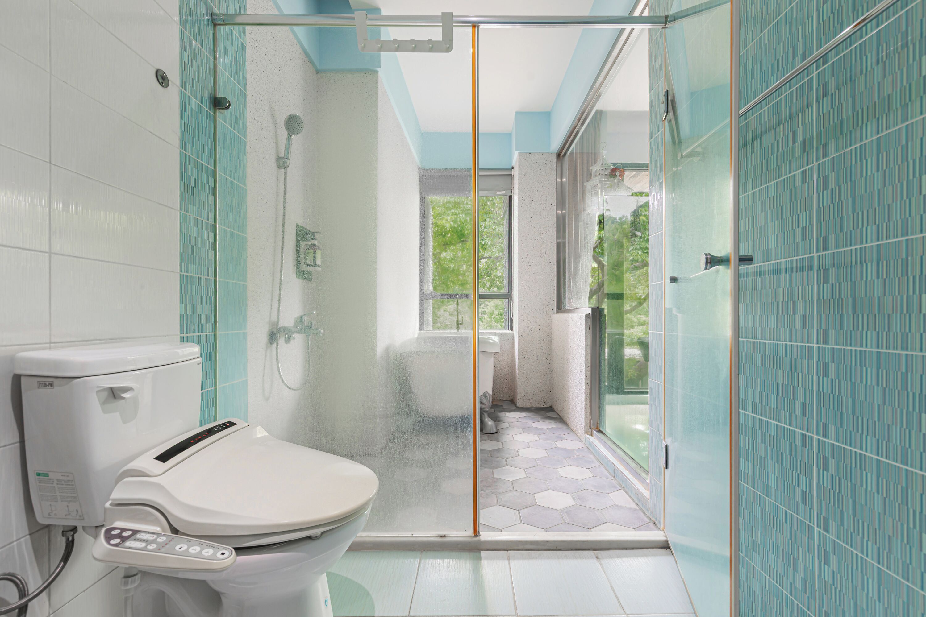 A modern bathroom with a toilet, shower, and glass door leading to a balcony.