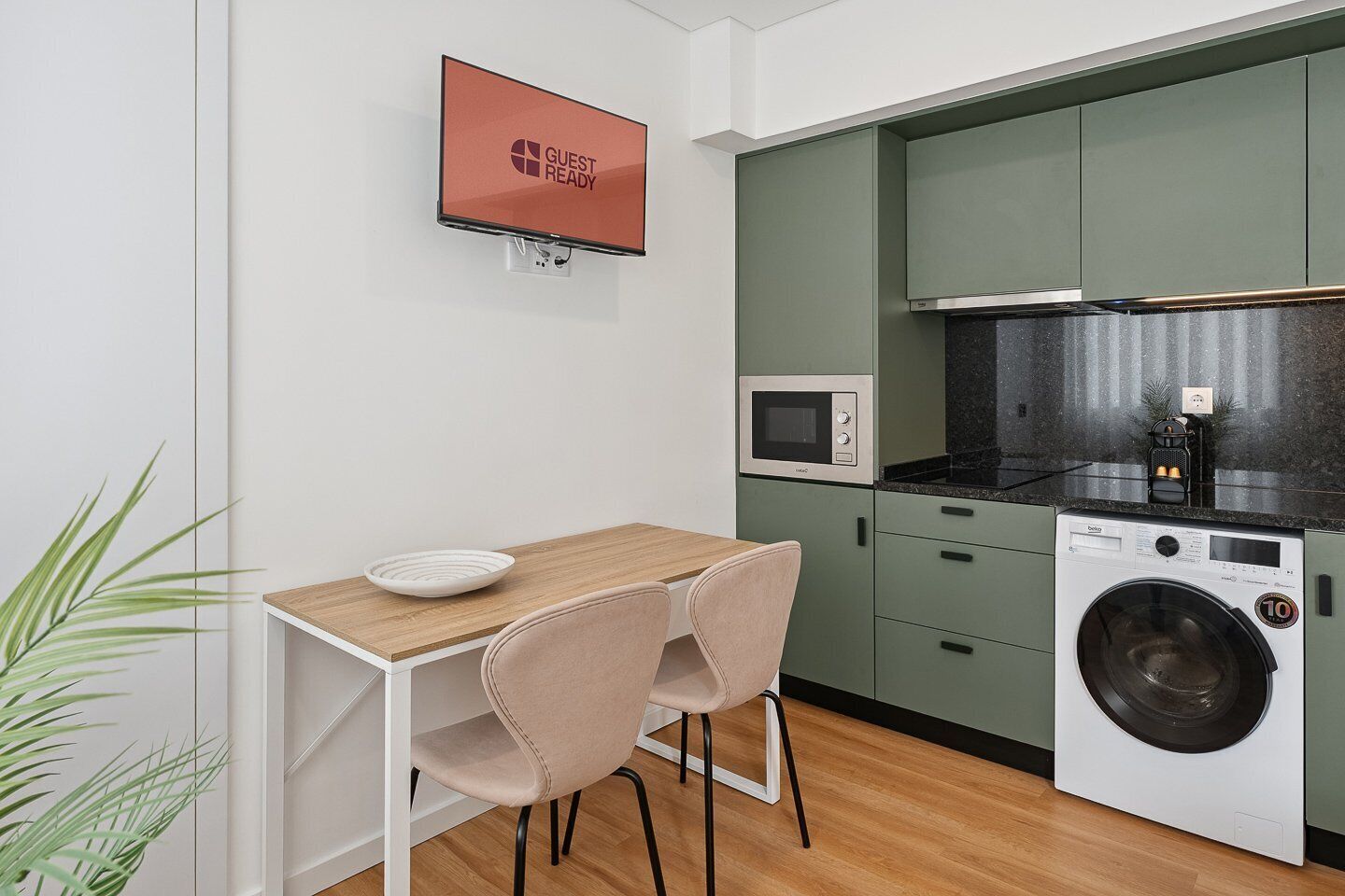 A compact kitchen with a microwave, washing machine, and a table with chairs.