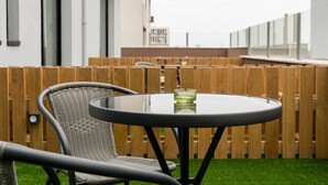 A round table with a glass top and a wicker chair in a patio area with a wooden fence and a building in the background. - GuestReady - Tutti Frutti Studio - Avocado (Porto)