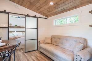 Une pièce dotée d’une porte-fenêtre coulissante, d’un canapé, d’une table en bois avec des chaises et d’une fenêtre donnant sur des arbres.