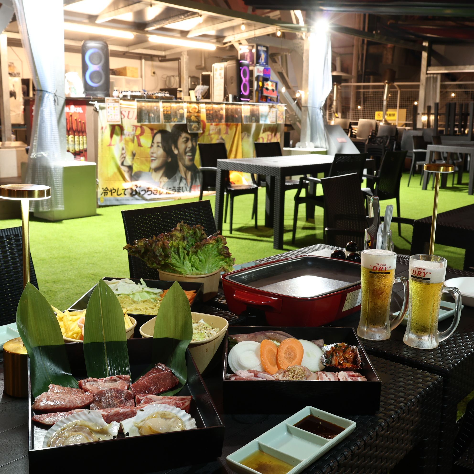 A dining area with a grill, various food items, and two glasses of beer.