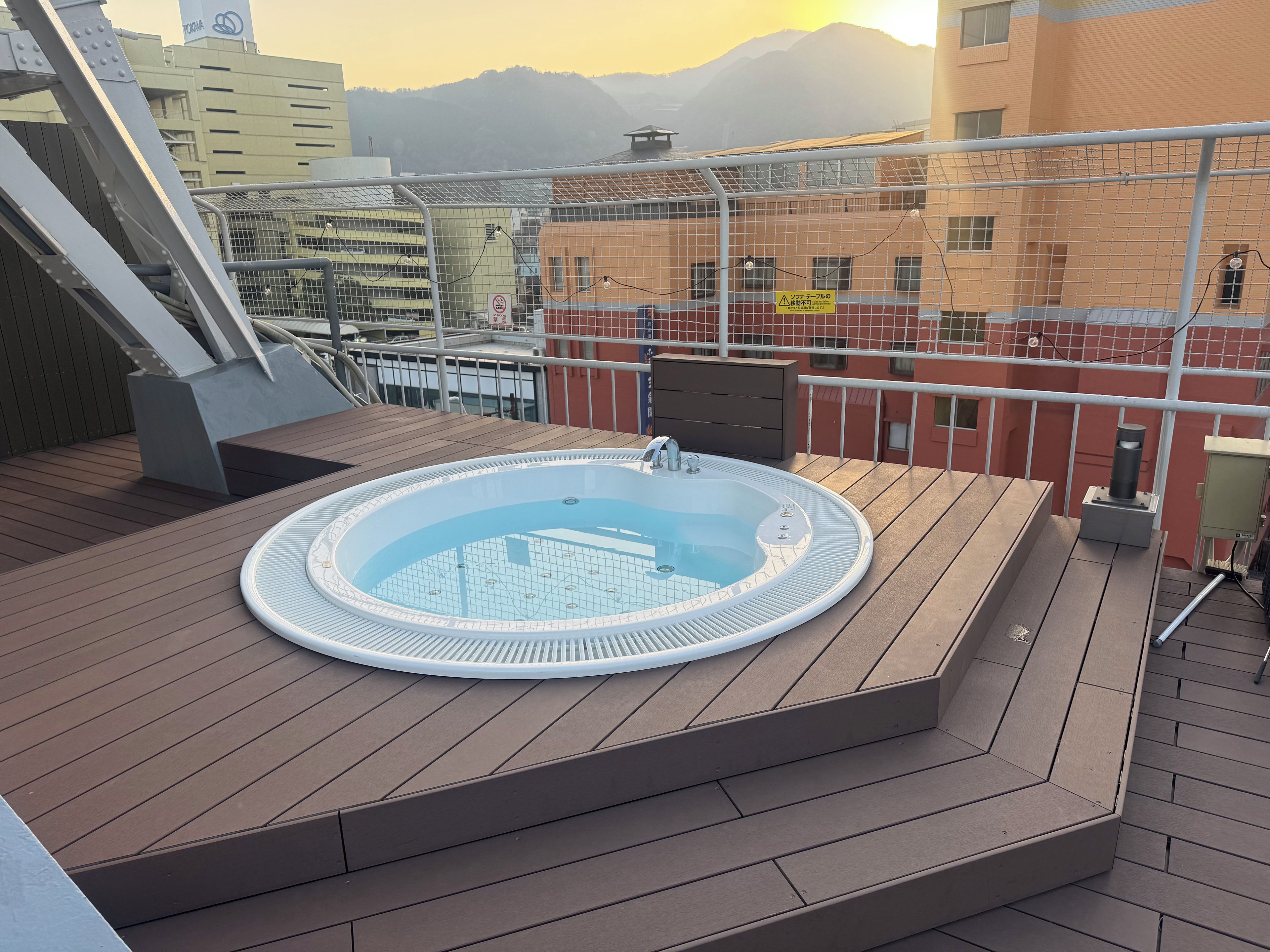 Une terrasse sur le toit avec un jacuzzi, une plateforme en bois et une vue sur les bâtiments et les montagnes.
