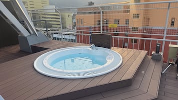 Une terrasse sur le toit avec un jacuzzi, une plateforme en bois et une vue sur les bâtiments et les montagnes.