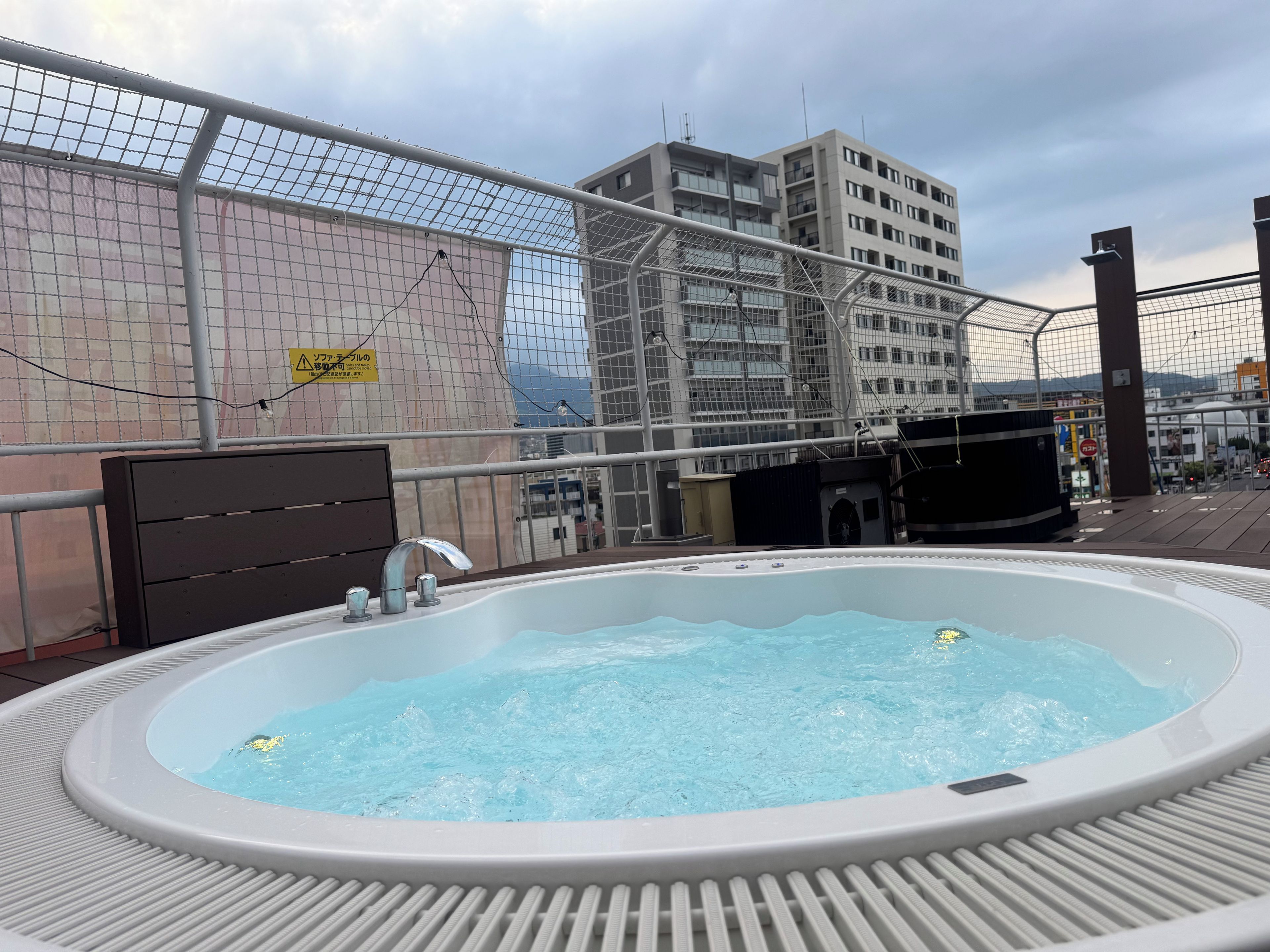 Un jacuzzi en una terraza en la azotea con vista a un paisaje urbano y un edificio en construcción.