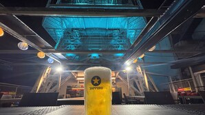 Ein Bierglas auf einem Tisch mit Metallgeländer und blauer Beleuchtung im Hintergrund.