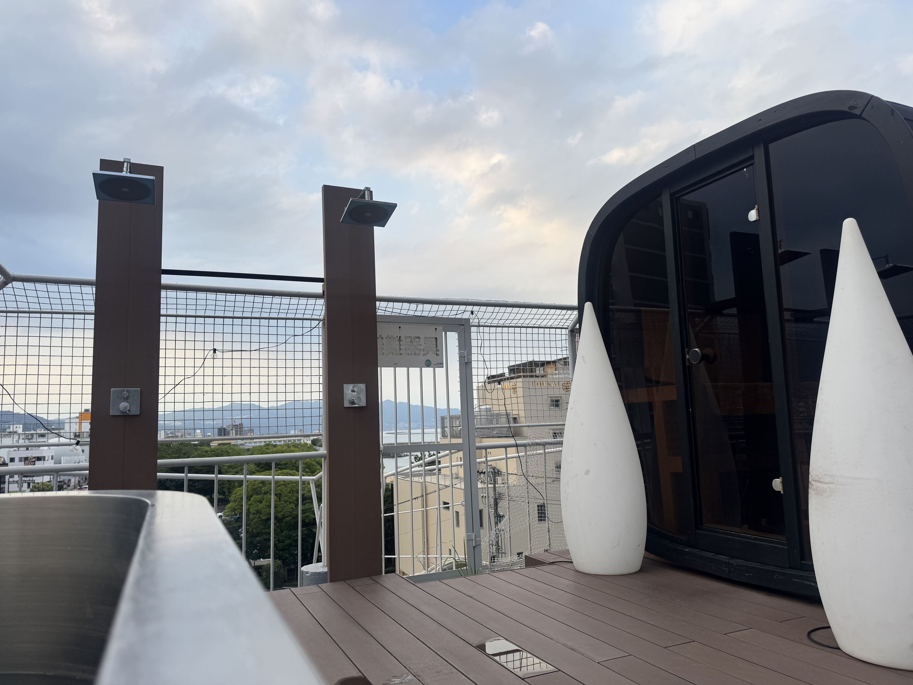 A balcony with a view of a cityscape, a glass door, and a white conical object.