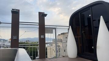 A balcony with a view of a cityscape, a glass door, and a white conical object.