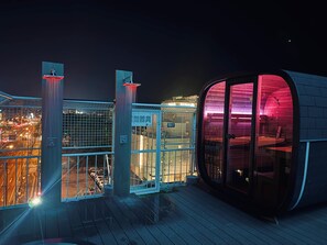 Un bâtiment moderne doté d’une façade en verre et d’une structure incurvée, illuminée de lumières rouges.