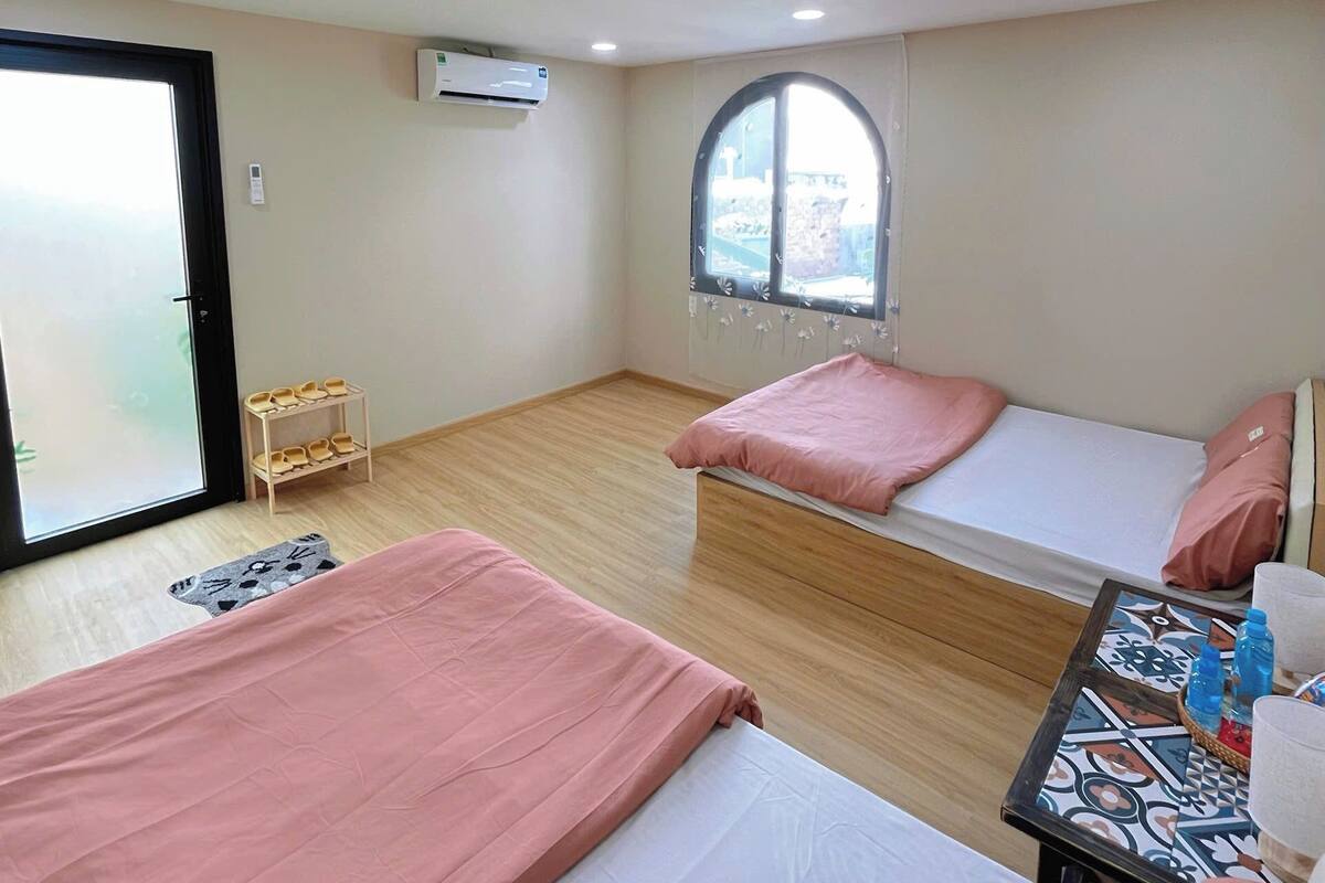 A room with two beds, a small table with bottles, and a window with a view.