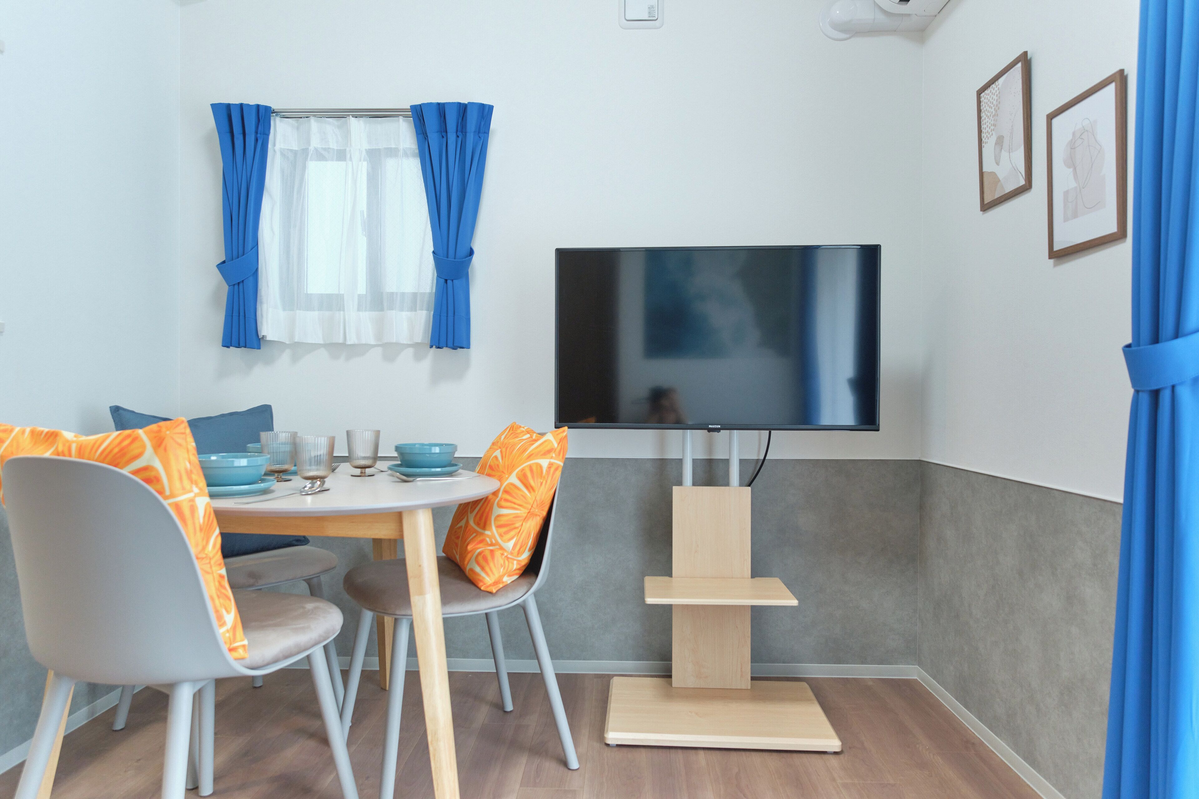 A modern room with a dining table, chairs, a TV, and a small wooden shelf.