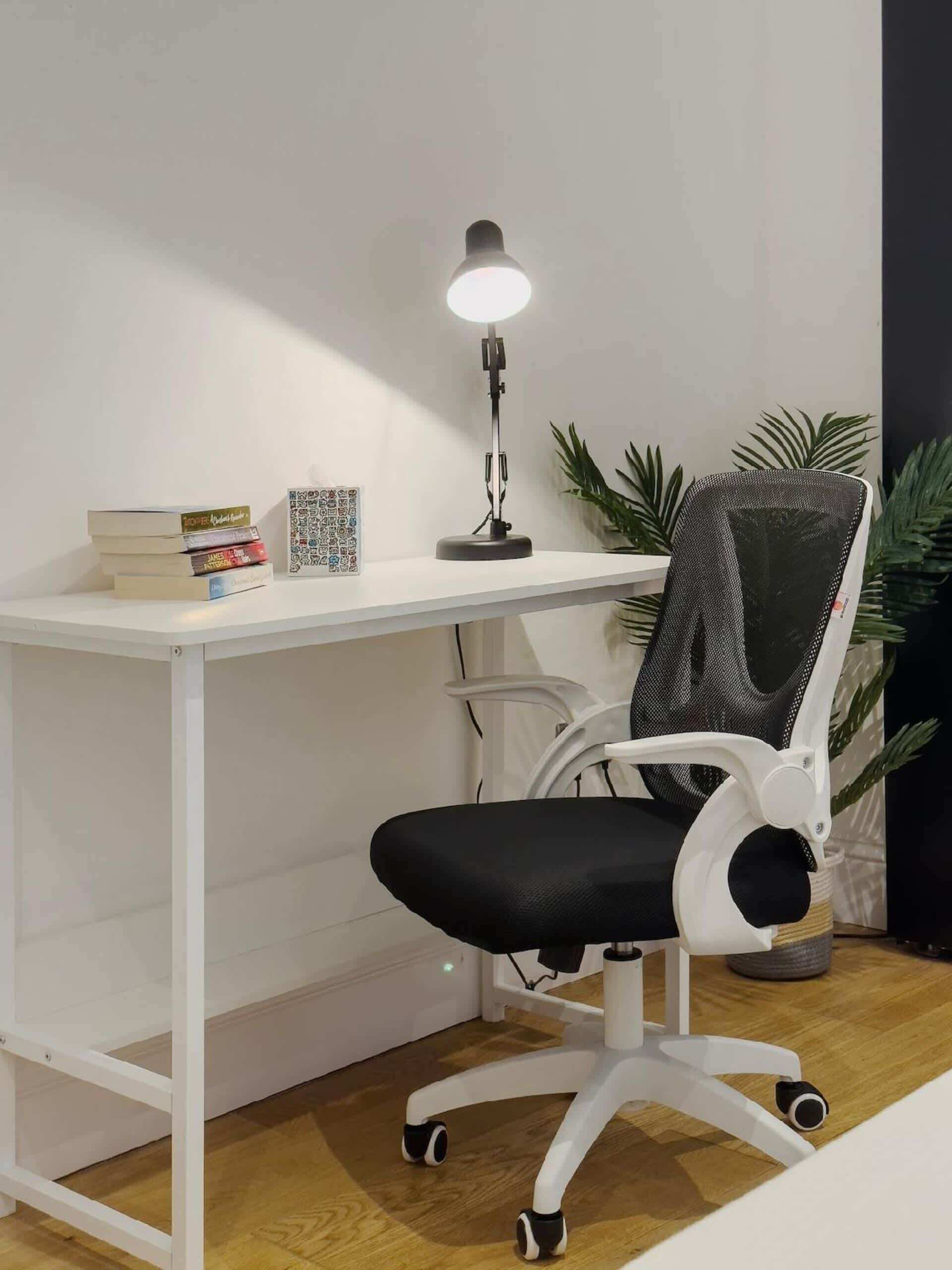 A white desk with a black office chair, a desk lamp, and some books.