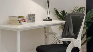 Un escritorio blanco con una silla de oficina negra, una lámpara de escritorio y algunos libros.