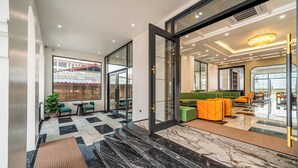 Un moderno vestíbulo de hotel con piso de mármol a cuadros, un sofá verde y asientos naranjas.