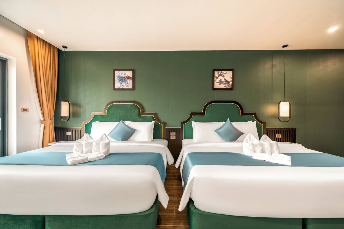 A hotel room with two beds, green walls, and framed artwork.