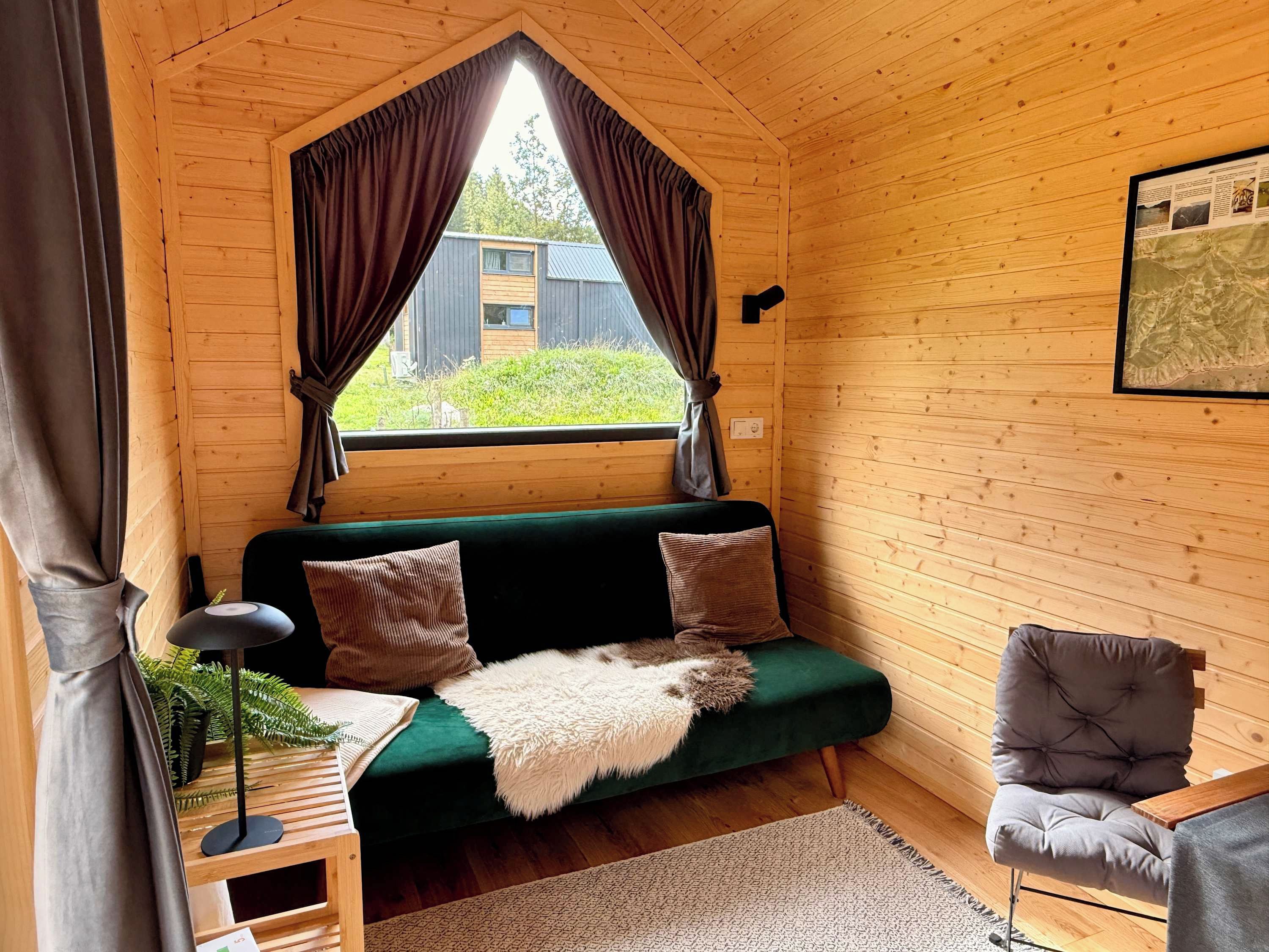 A cozy cabin interior with a green sofa, a chair, a small table, and a window with curtains.