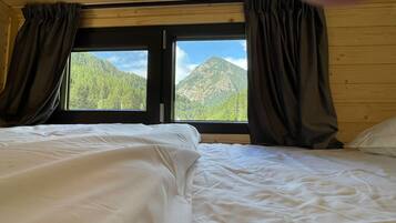A room with two beds, a window with curtains, and a view of mountains.