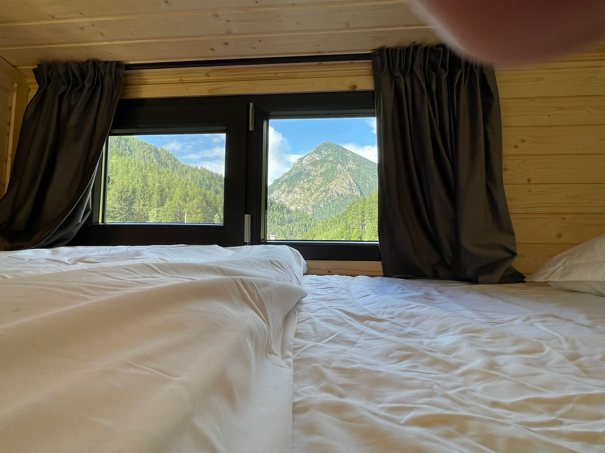 A room with two beds, a window with curtains, and a view of mountains.