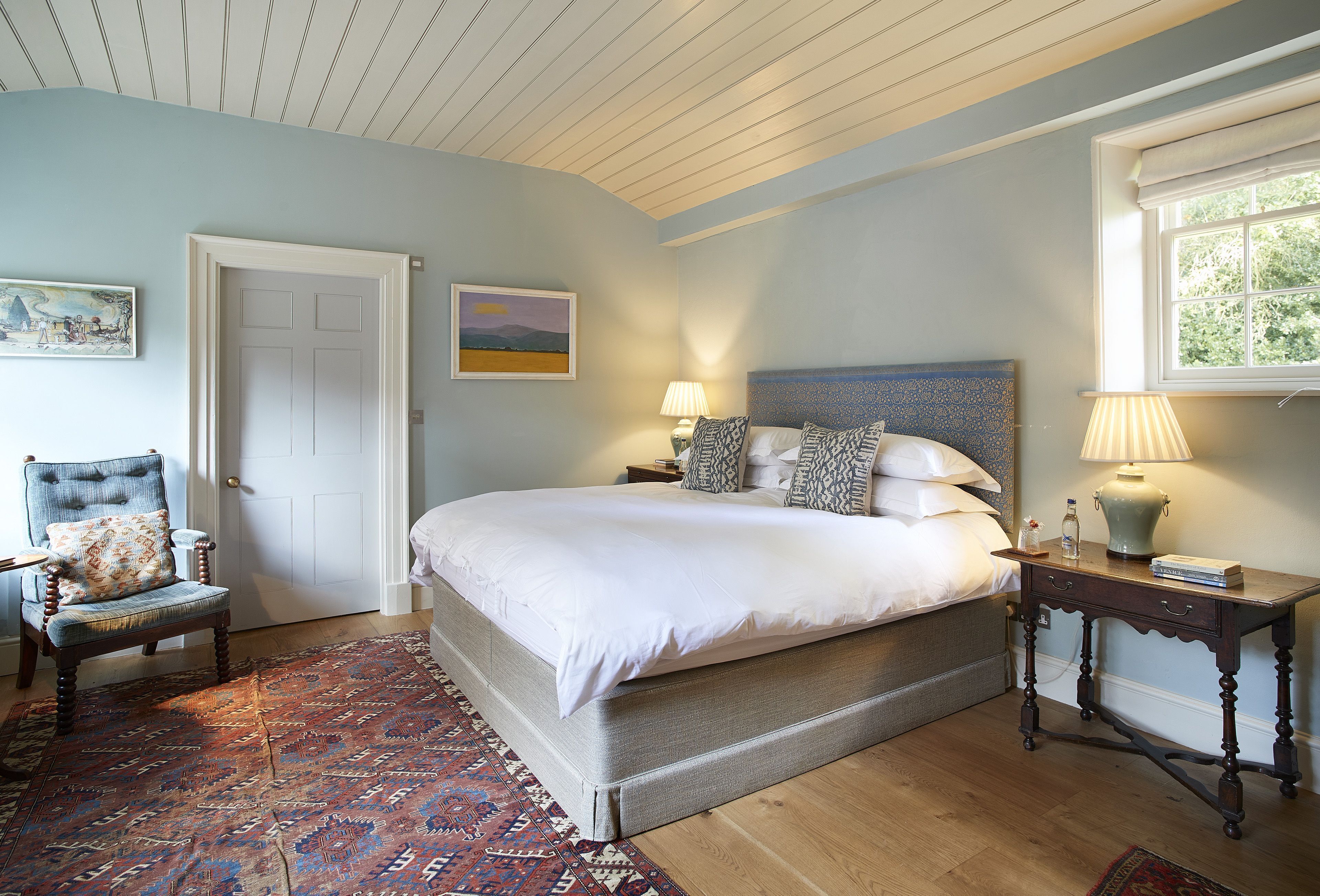 Een slaapkamer met een groot bed, een stoel, een nachtkastje en een raam.