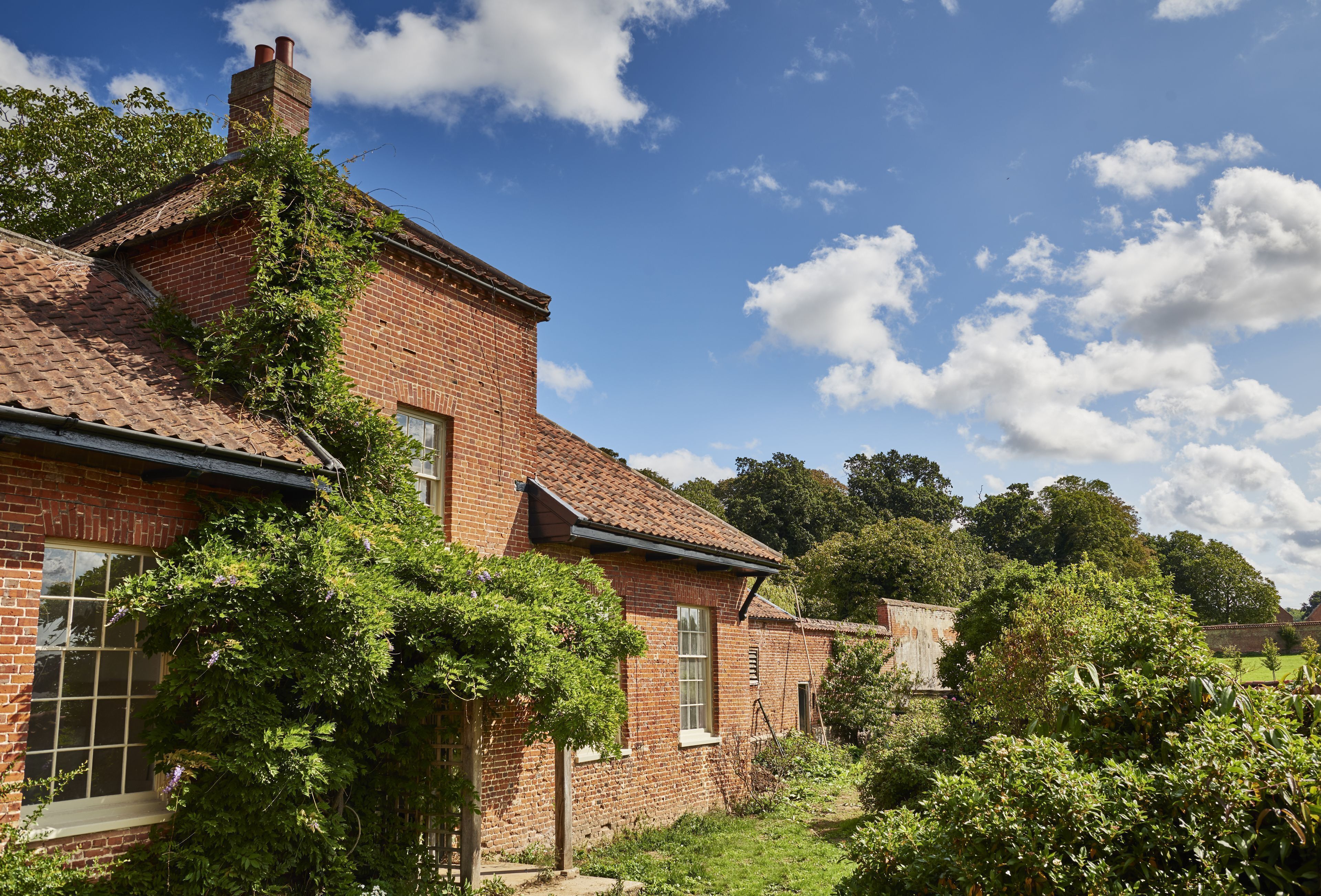 A brick house with a tiled roof, surrounded by lush greenery and trees.