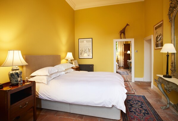 A bedroom with a large bed, two bedside tables with lamps, a radiator, and a door leading to another room.