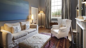 A living room with a sofa, armchair, ottoman, and a large painting on the wall.