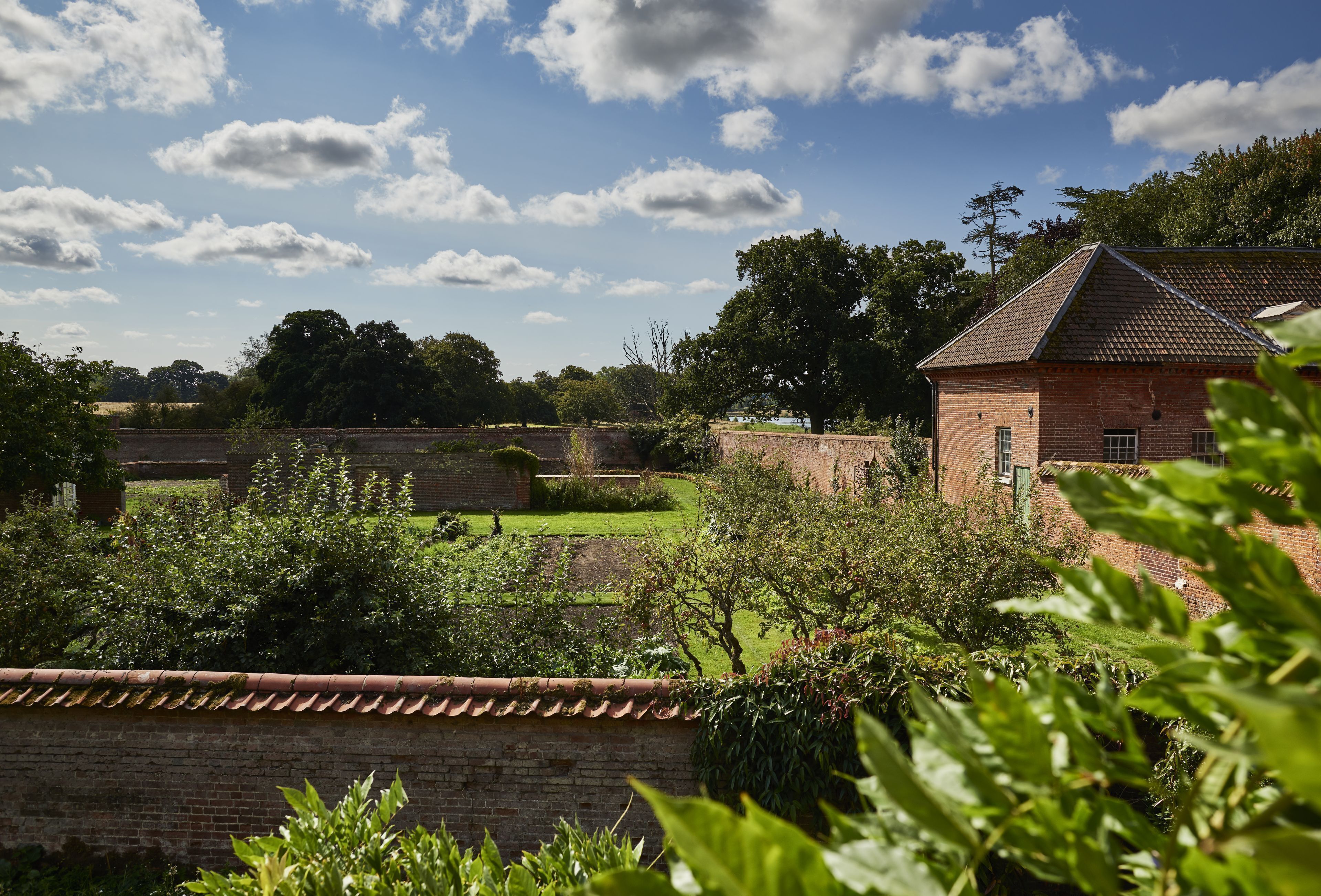 A brick building with a tiled roof, surrounded by a well-maintained garden and a brick wall.