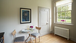Un comedor con una mesa preparada para dos, una obra de arte enmarcada en la pared y una ventana con flores.