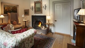 Una sala de estar acogedora con chimenea, un sillón cómodo, un sofá con tapicería floral y una puerta de madera tradicional.