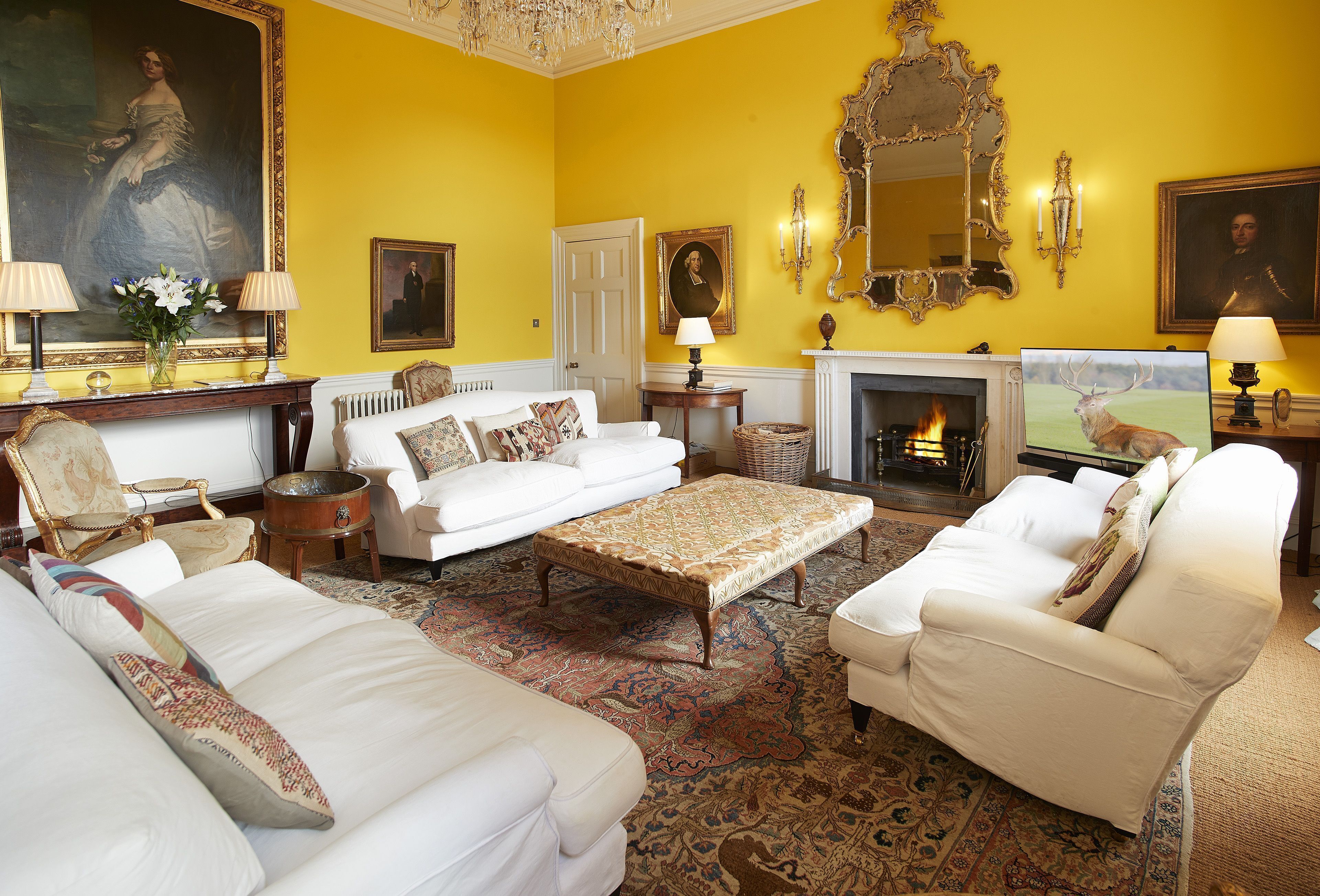A room with a fireplace, white sofas, a patterned rug, and a large portrait on the wall.