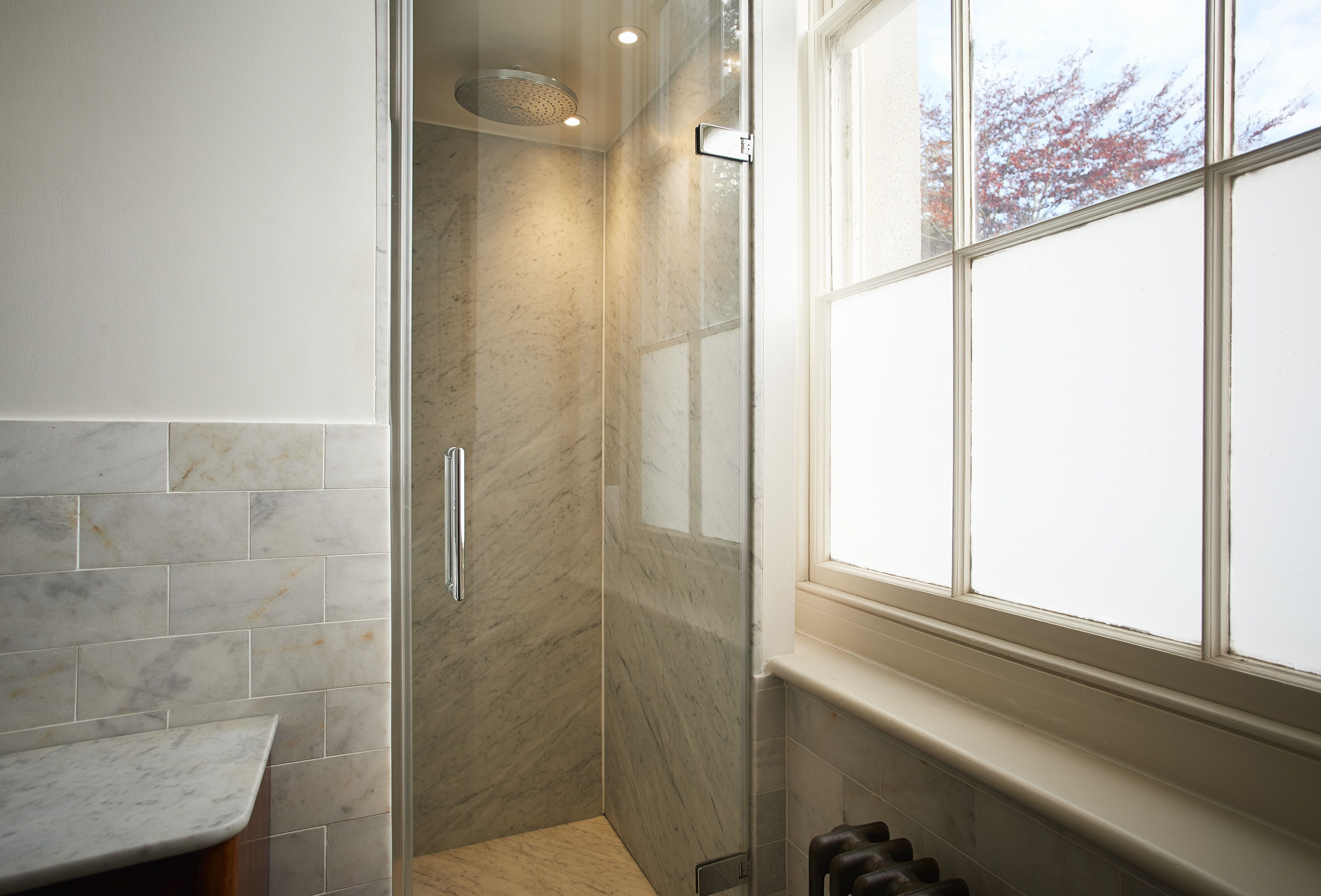 Un bagno con cabina doccia in vetro, parete rivestita in marmo e finestra che offre luce naturale.
