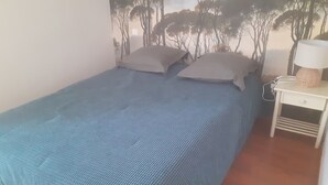 A single-bed room with a blue textured bedspread, a nightstand with a lamp, and a wall mural of trees. - CORBIERES HOUSE NEAR LAGRASSE (Saint-Pierre-des-Champs)