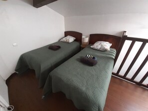 Una stanza con due letti singoli, ognuno con copriletto e cuscini verdi, un comodino con una lampada e una sedia di legno.
