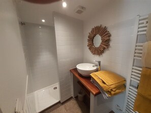 Un bagno con un lavandino bianco, un piano di lavoro in legno, un portasciugamani e uno spazio doccia.