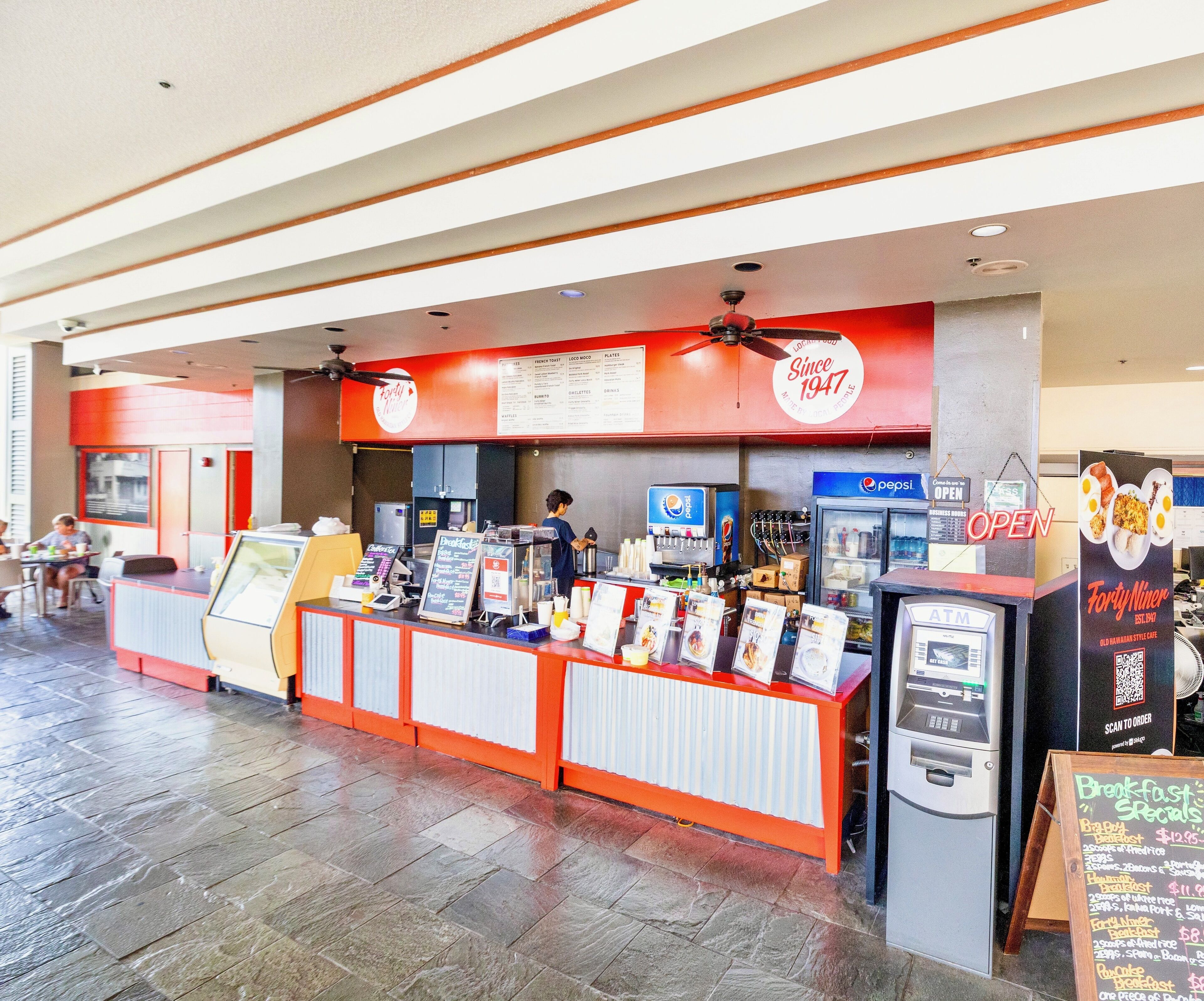 A fast-food restaurant with a counter, menu boards, and an ATM.