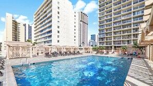 A swimming pool with lounge chairs and umbrellas, surrounded by tall buildings.