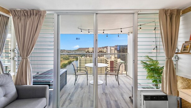 A balcony with a sliding glass door, a round table with chairs, a sofa, a potted plant, and string lights.