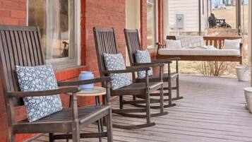 A covered porch with wooden rocking chairs and a bench, brick walls, and a view of the backyard.