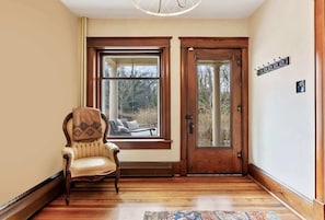 Une pièce avec un plancher en bois, une chaise, une grande fenêtre et une porte.