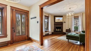 Een ruime woonkamer met houten vloeren, een open haard en een groene bank.