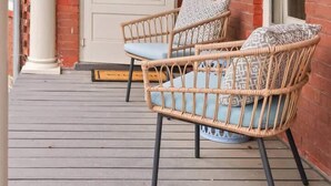 Een veranda met twee rieten stoelen en een witte deur.