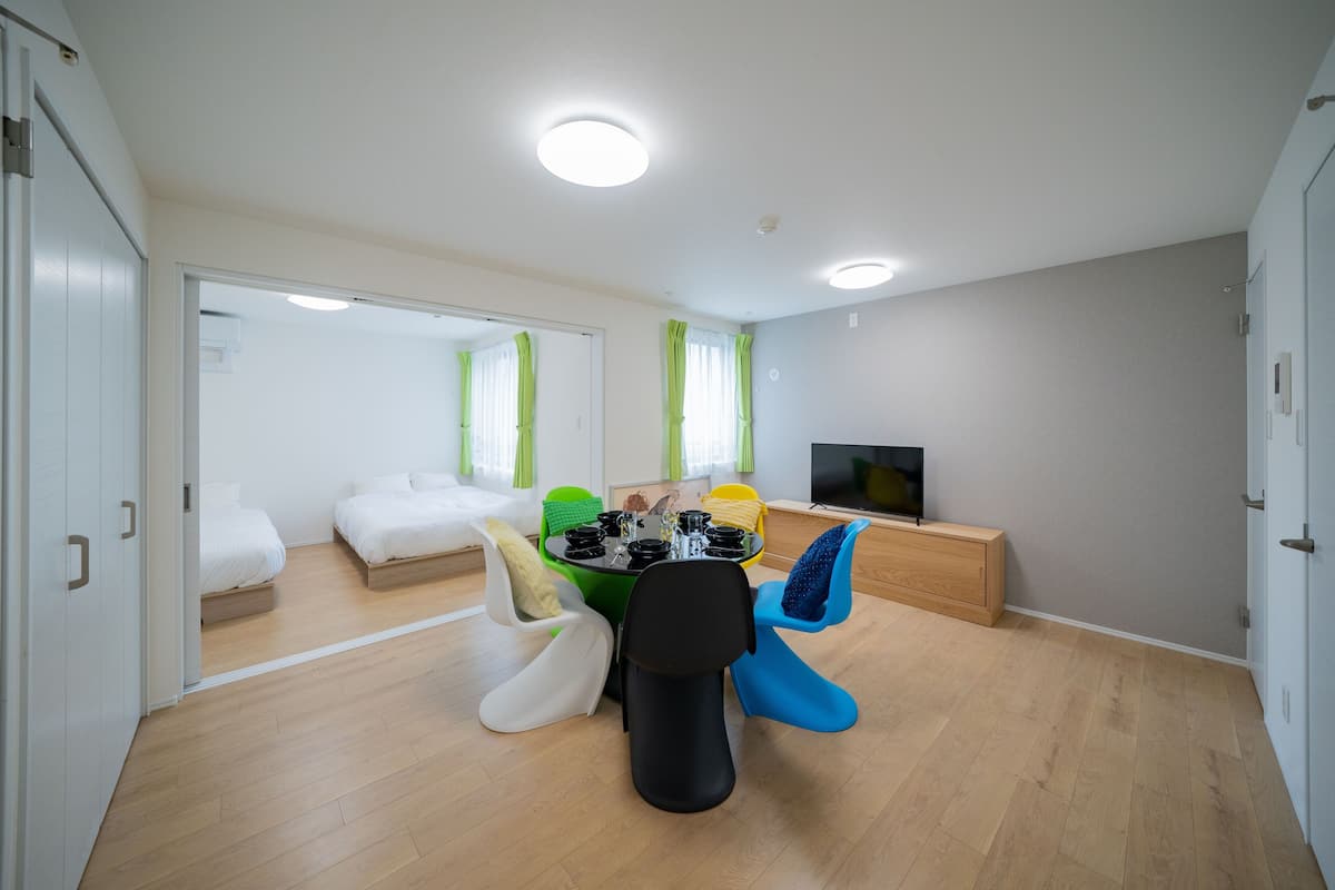 A modern, well-lit room with a dining table, chairs, a TV, and a bed.