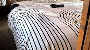 Una cama con ropa de cama a rayas y un cabecero, una mesita de noche y un espejo.