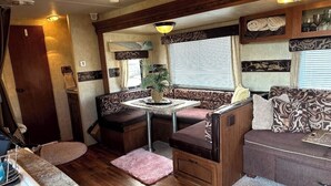 Interior compacto de autocaravana con kitchenette, comedor y zona de estar con sofá y bancos acolchados.